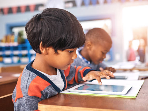 istock Tablet, school and child with books in classroom for online learning, studying and knowledge. Education, academy and young boy with textbooks and digital tech for lesson, development and research 2160069392