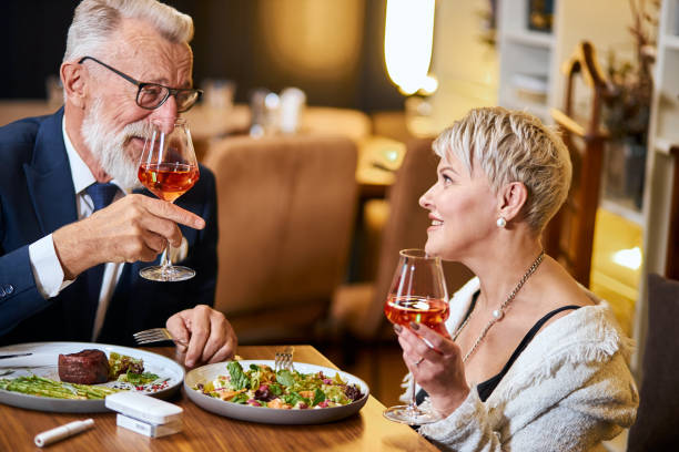 istock Stylish senior couple taking meal in restaurant, using electronic cigarette. IQOS 2160069605