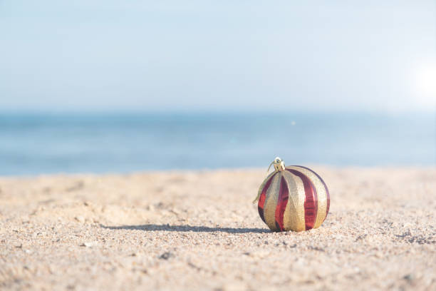 celebrating Christmas in hot countries. Christmas decorations bauble ball on sandy beach with sea background. copy space