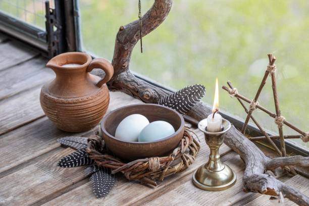 istock Home pagan spring altar with willow wreath, clay jug with milk, eggs, burning candle and birds feathers on wooden surface, selected focus. 2160084655