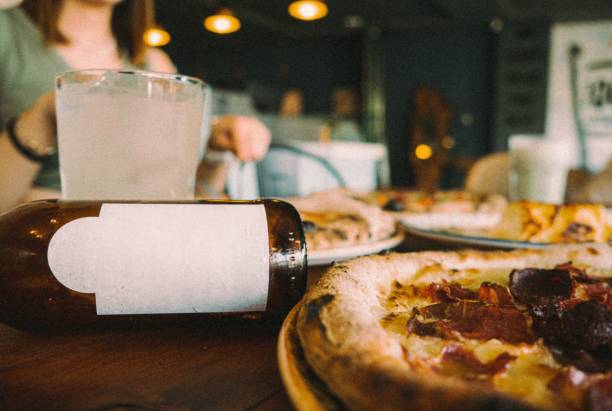 Pizzas on the table, beverage standing on the front and a customer trying the pizza