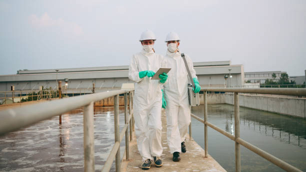 istock Two Environmental Engineers in Safety PPE Suits Work at Wastewater Treatment Plants, Employees check water quality in wastewater treatment plants. 2160086611