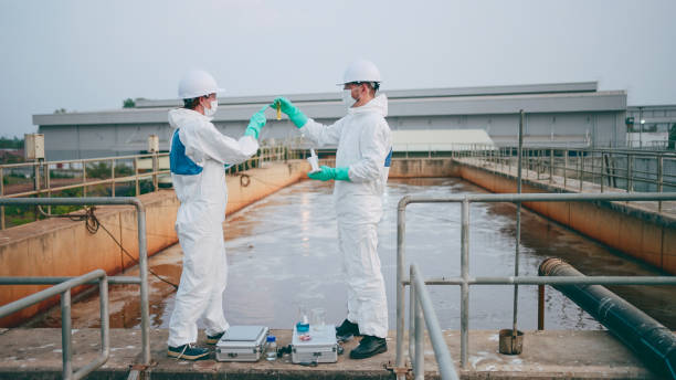 istock Two Environmental Engineers in Safety PPE Suits Work at Wastewater Treatment Plants, Employees check water quality in wastewater treatment plants. 2160086742