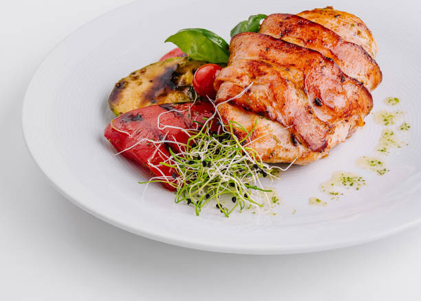 Juicy grilled chicken breast with grilled vegetables, garnished with microgreens on a white plate