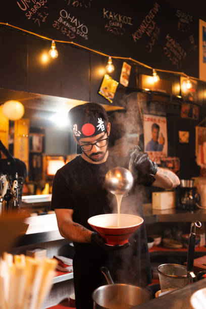istock Skilled chef pours savory broth into a bowl, crafting a delectable ramen dish in a restaurant 2160096851