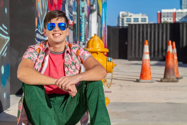 Portrait of young latin college university happy handsome male student, skater, Art Director, Graphic Designer, Designer; enjoying his time in the United States taking a look around graffitis and installations arts in Wynwood District Miami Design District, Miami neighborhood while doing skateboarding.
He's wearing a colorful outfit: Tropical shirt, pink t-shirt and green jeans.
Redefining masculine beauty and fashion concept. Copy Space. retrato de joven latino universidad feliz guapo estudiante masculino, patinador, director de arte, diseñador gráfico, diseñador disfrutando de su tiempo en los estados unidos echando un vistazo alrededor de graffitis e instalaciones artísticas en wynwo
