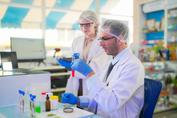 Close-up of a female scientist wearing protective gear, closely inspecting genetically modified plants in a laboratory setting. The image represents biotechnology, genetic engineering, and scientific research related to GMO crops and agriculture.