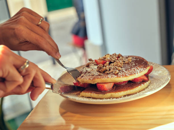 Crop anonymous person cutting tasty sweet pancakes with chocolate paste and strawberries while sitting at table in cafe during breakfast time