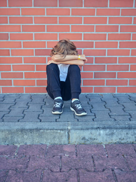 istock Unrecognizable boy hugging knees and sitting near brick wall 2160111248
