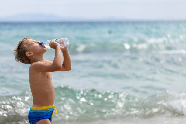istock Caucasian boy drinking water from the water bottle, on the beach 2160111742
