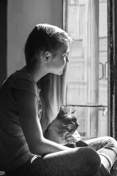 istock girl with cat looking through the window 2160117421