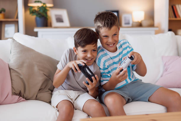 istock Boys sitting on sofa, playing video games and smiling 2160125541