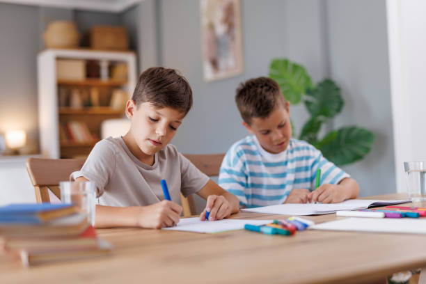 istock Two boys focused on writing at a wooden table. 2160125822