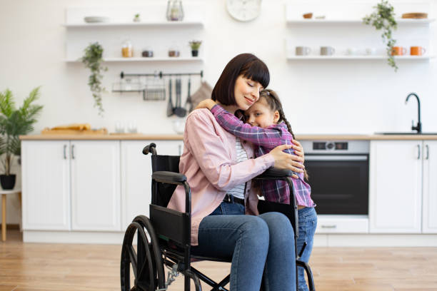 istock Caring mother in wheelchair hugging her daughter in kitchen 2160132152