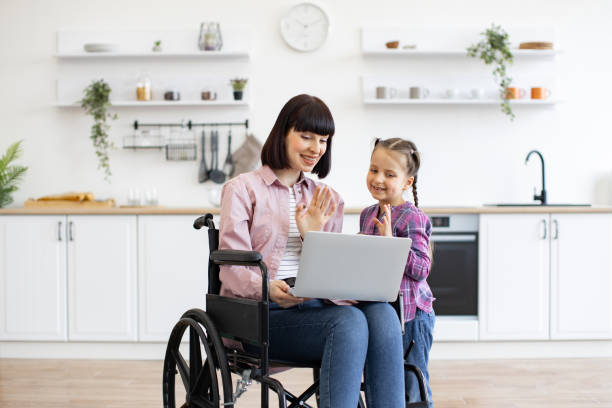 istock Mother in wheelchair with daughter using laptop in modern kitchen 2160132160