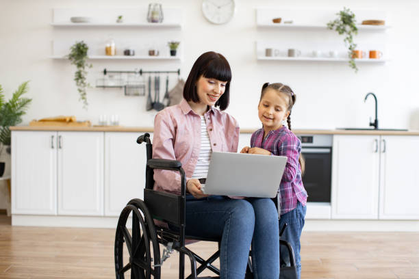 istock Mother in wheelchair with daughter using laptop in kitchen 2160132177