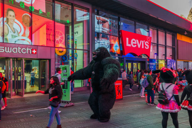 View of busy street in Times Square, featuring people in costumes, including gorilla suit, outside Swatch and Levi's stores with bright lights and advertisements. New York. USA. 06.30.2024. View of busy street in Times Square, featuring people in costumes, including gorilla suit, outside Swatch and Levi's stores with bright lights and advertisements. retail digital signage stock pictures, royalty-free photos & images