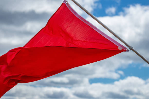 istock Red warning flag flying in the wind against blue sky 2160137338