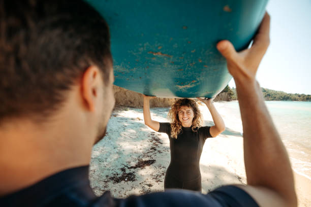 Couple carrying paddle board on the beach