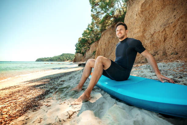 istock Young smiling man sitting on a paddleboard at the beach 2160139899