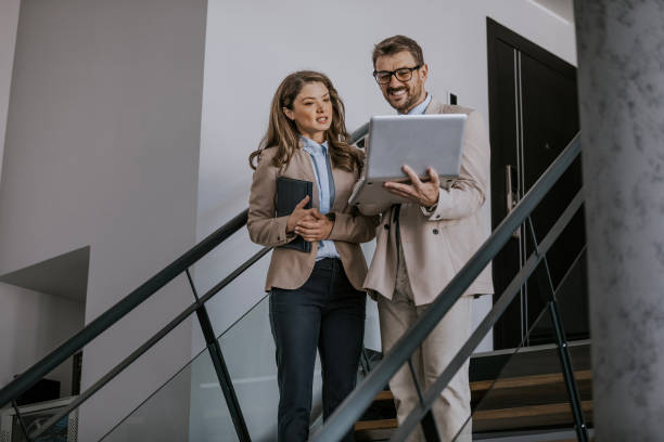 istock Business colleagues discuss project on laptop while walking down stairs in modern office building 2160143298