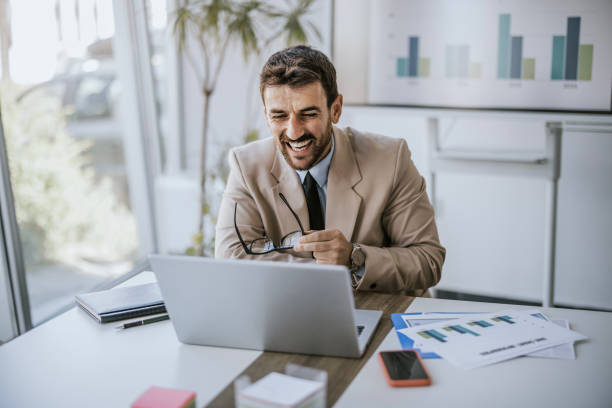 istock Businessman working on laptop while laughing in modern office during daytime 2160144359