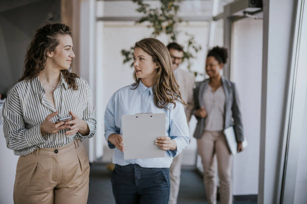 istock Two businesswomen walking and talking in modern office hallway 2160144442