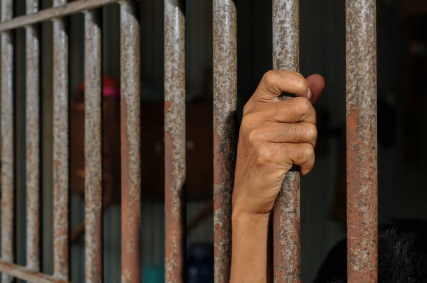 istock hands of a prisoner behind prison bars on black background 2160152352