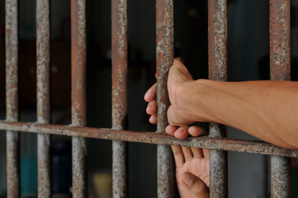 istock hands of a prisoner behind prison bars on black background 2160152353