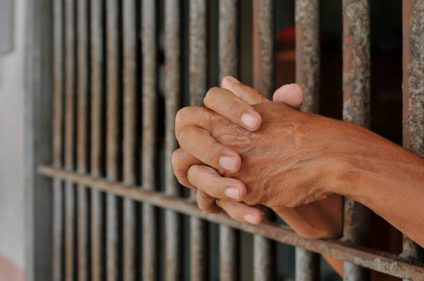 istock hands of a prisoner behind prison bars on black background 2160152381