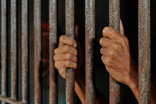 istock hands of a prisoner behind prison bars on black background 2160152698