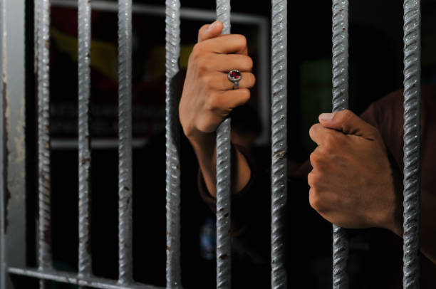 istock hands of a prisoner behind prison bars on black background 2160152700