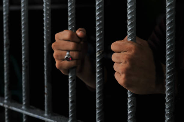 istock hands of a prisoner behind prison bars on black background 2160152731