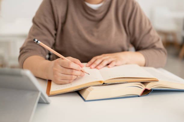 istock A close-up image of a female student using her digital tablet and researching information in a book. 2160171990