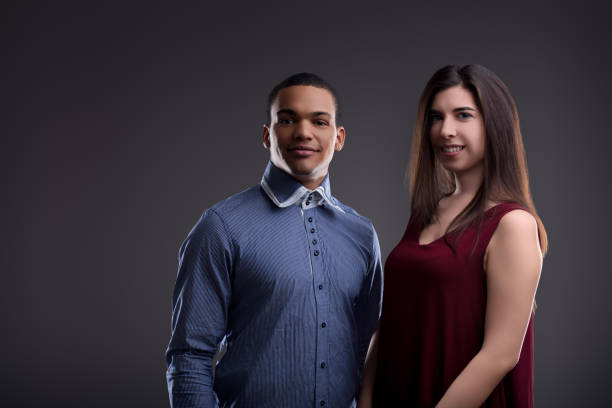 Young multiethnic couple in smart casual outfits, smiling and looking at the camera on a neutral background, radiating happiness and love with their trendy fashion choices