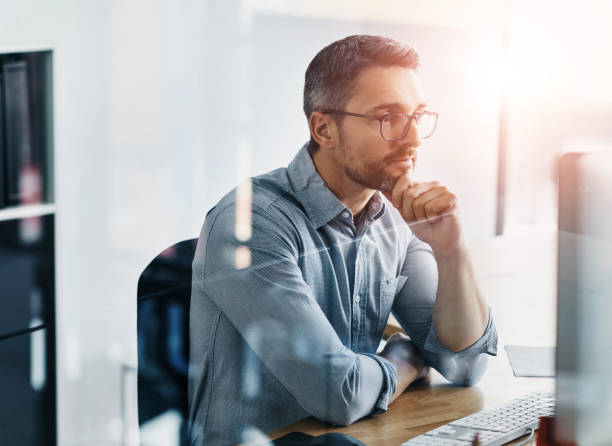 istock Thinking, computer and businessman in office reading information on stock exchange for investment. Ideas, research and male financial analyst planning company budget with online report on desktop. 2160190415