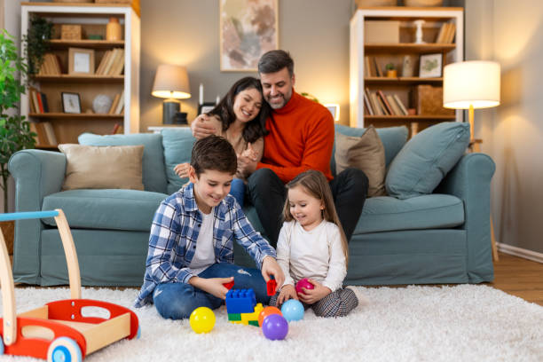 istock Cute kids playing while parents relaxing sofa at home together, smiling active boy entertaining with toy car near his sister on floor, happy family spending time together in living room on weekend 2160190682