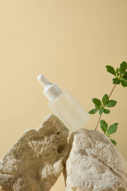 istock A white serum bottle without label displayed on stone pedestal, dotted by green tree branch on the right, over light yellow background. Cosmetic mock up with space for designing 2160193435