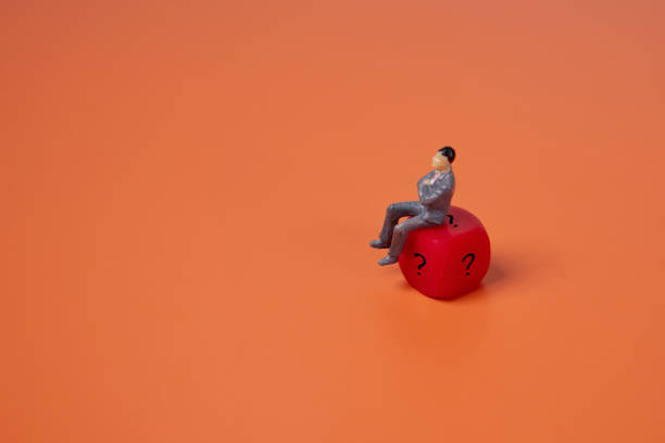 istock Businessman sitting on red dice with a question mark on orange background. 2160194256