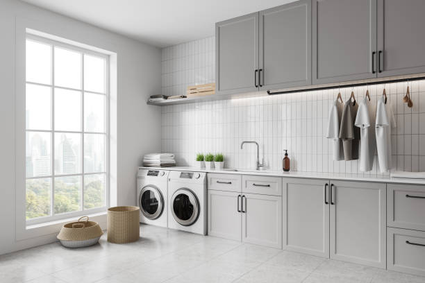 istock Grey home laundry interior with washing cabinet and clothes, panoramic window 2160201392