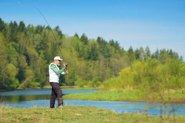 istock Fisherman with a spinning rod catching fish on a river at sunny summer day with green trees at background. 2160201416