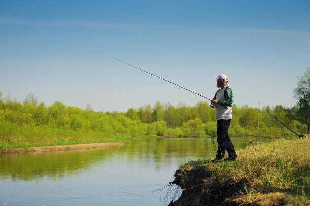 istock Fisherman with a spinning rod catching fish on a river at sunny summer day with green trees at background. 2160201434
