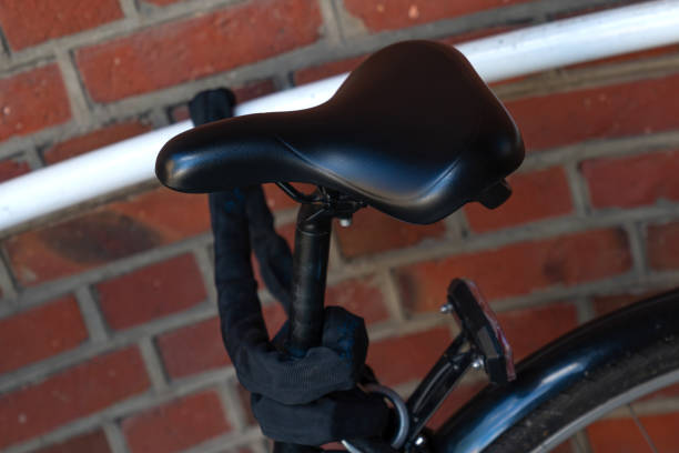 A black bicycle seat is leaning against a brick wall. The seat is covered in a black material, and the bicycle frame is visible in the background. There is a white pipe behind the bicycle, and the sun is shining brightly. The image captures a moment of simple beauty in an everyday object.