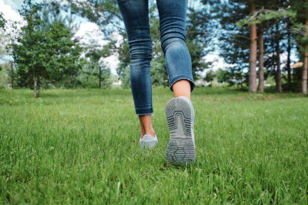 Rear view of female legs in jeans and sneakers walking on grass