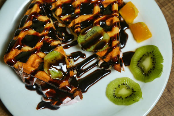 A plate of waffles drizzled with chocolate sauce and topped with kiwi and orange slices.