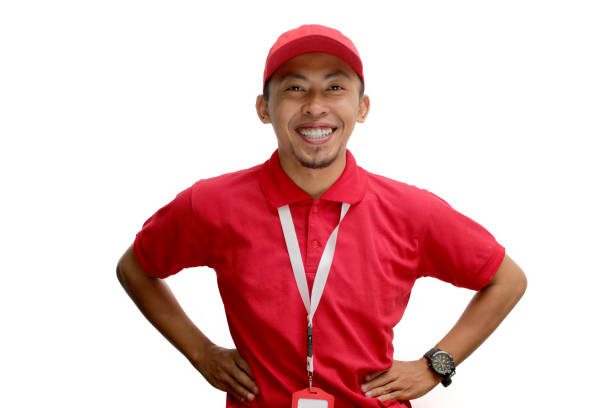 Confident Asian delivery man or courier stands with his hand on his hip in an arm akimbo gesture, isolated on white background. Concept of reliability, trustworthiness, logistics and delivery services