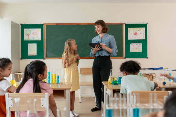 istock Adorable student learn with teacher in classroom at elementary school. Group of young schoolboy and girl sit on table, study science and doing chemistry experiment with fun activity at kindergarten. 2160219118