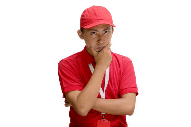 Asian delivery man or courier is deep in thought, putting his hand on his chin in a thinking gesture. Isolated on a white background, this image captures a moment of contemplation and concentration.