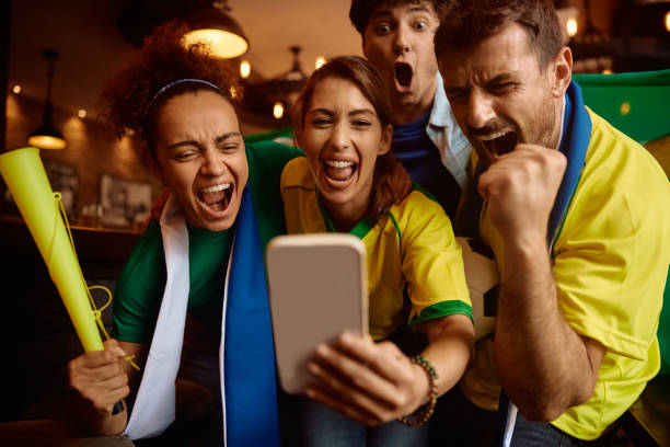 istock Group of sport fans shouting while using cell phone and cheering for their favorite team. 2160226594