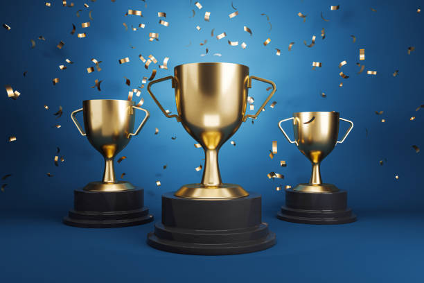 istock Three golden trophies with falling confetti on a blue background, symbolizing achievement and victory. 3D Rendering 2160228555